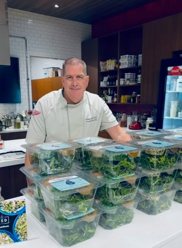 Chef standing behind stacks of Planted Detroit salad bowls in a modern kitchen.