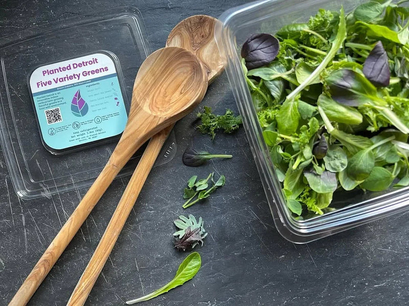 Planted Detroit Five Variety Greens Mix with fresh leafy greens and wooden salad servers.