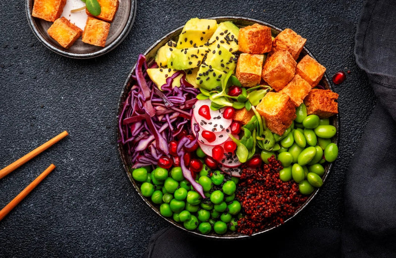 A  bowl of colorful vegetables like edamame, peas, etc., with a pair of chopsticks beside it.