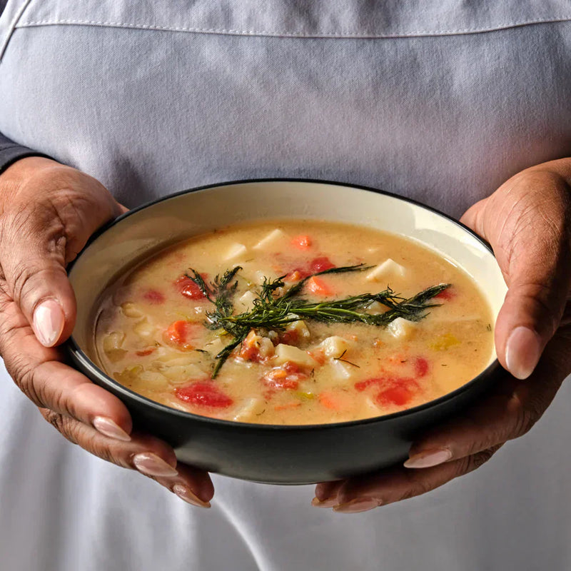 Hands holding a warm creamy vegetable soup garnished with microgreens, made with fresh Planted Detroit produce for a cozy Valentine’s dinner.