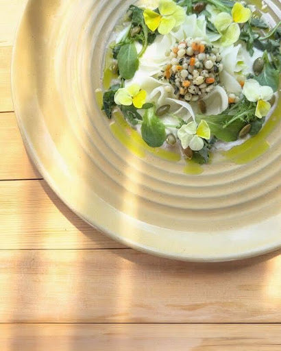 Planted Detroit salad topped with microgreens and edible flowers, drizzled with olive oil on a white platter.